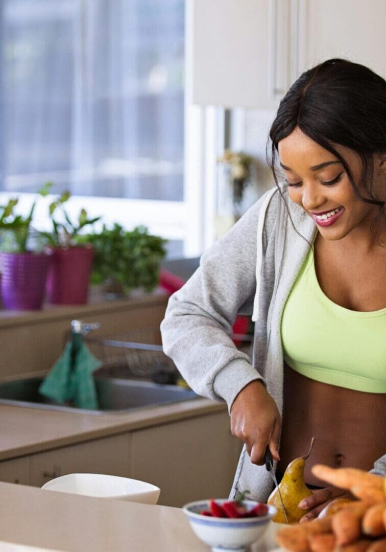 A woman cutting fruit in the kitchen with bananas and carrots.